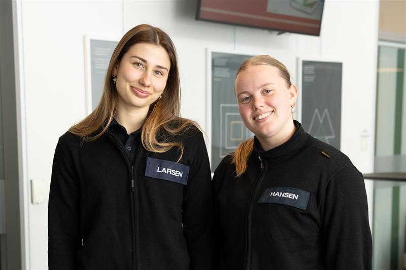 To uniformerte kvinnelige studenter smiler mot kamera. Foto