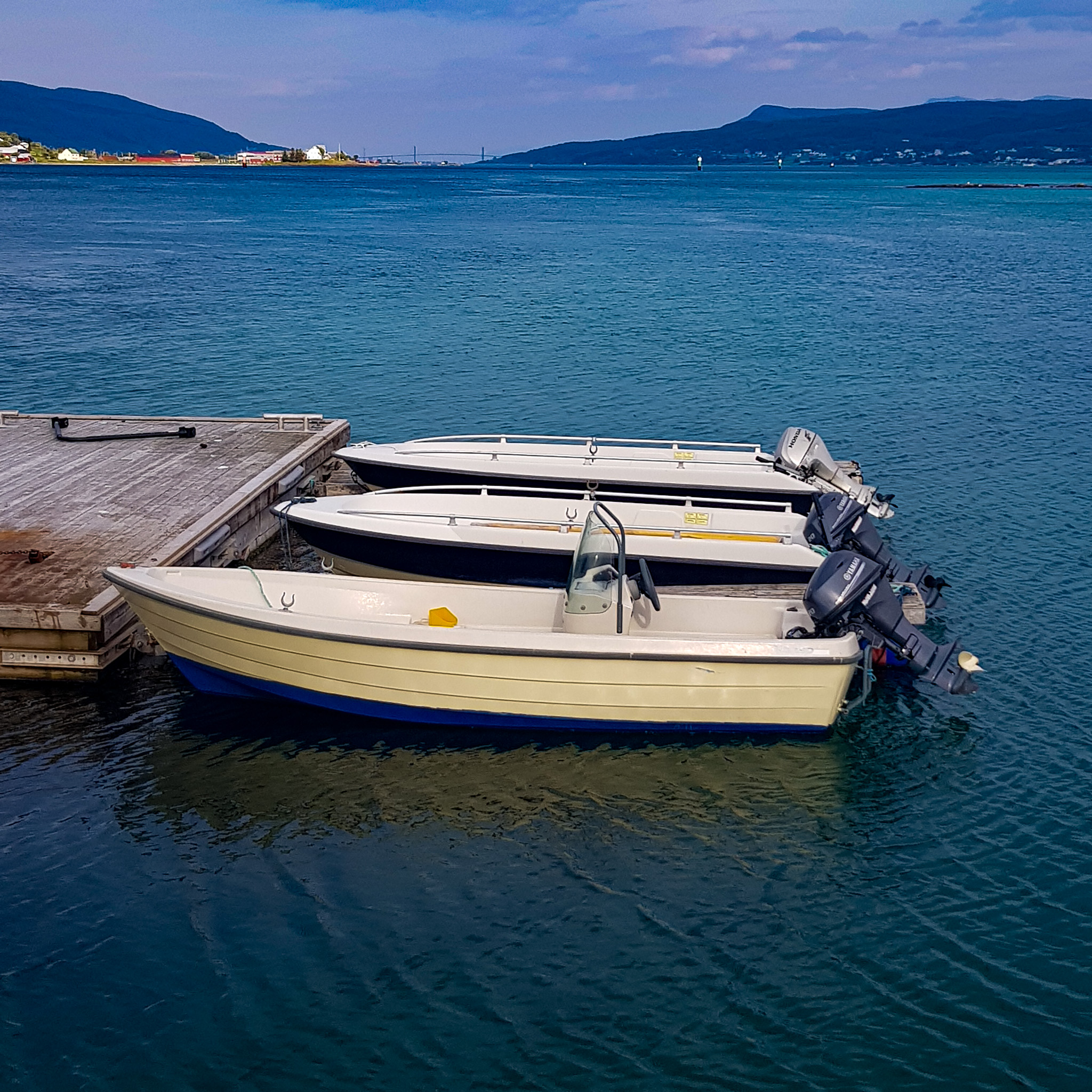 Tre motorbåter ligger til kai. Blått hav og fjell i bakgrunnen
