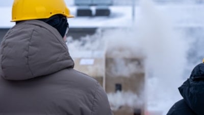 Mann med ryggen til kamera observerer røyk fra et modellhus. Foto