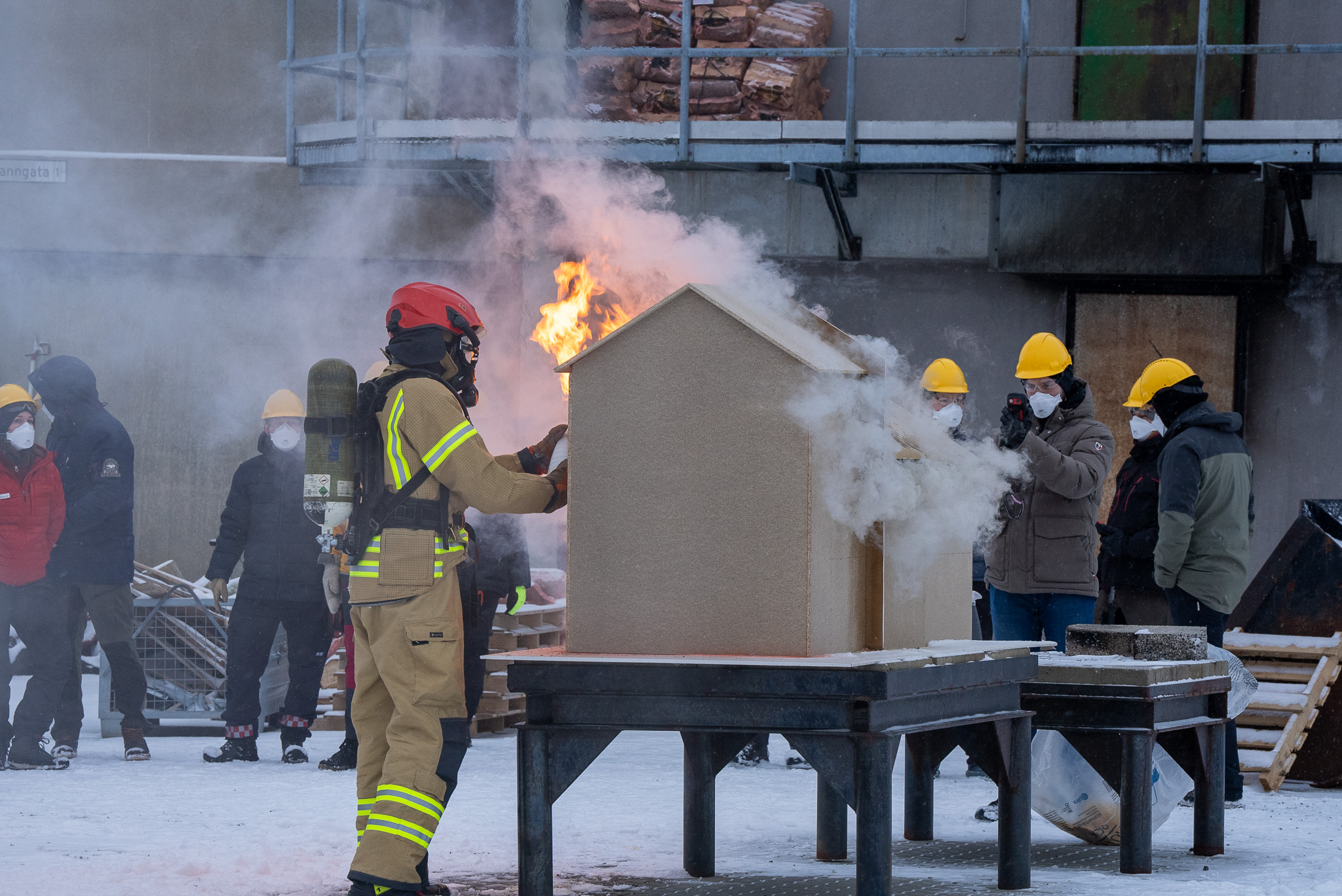 Brannkonstabel står ved et modellhus som brenner. Foto