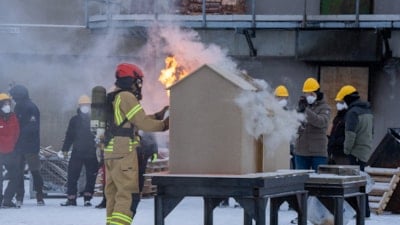 Brannkonstabel står ved et modellhus som brenner. Foto