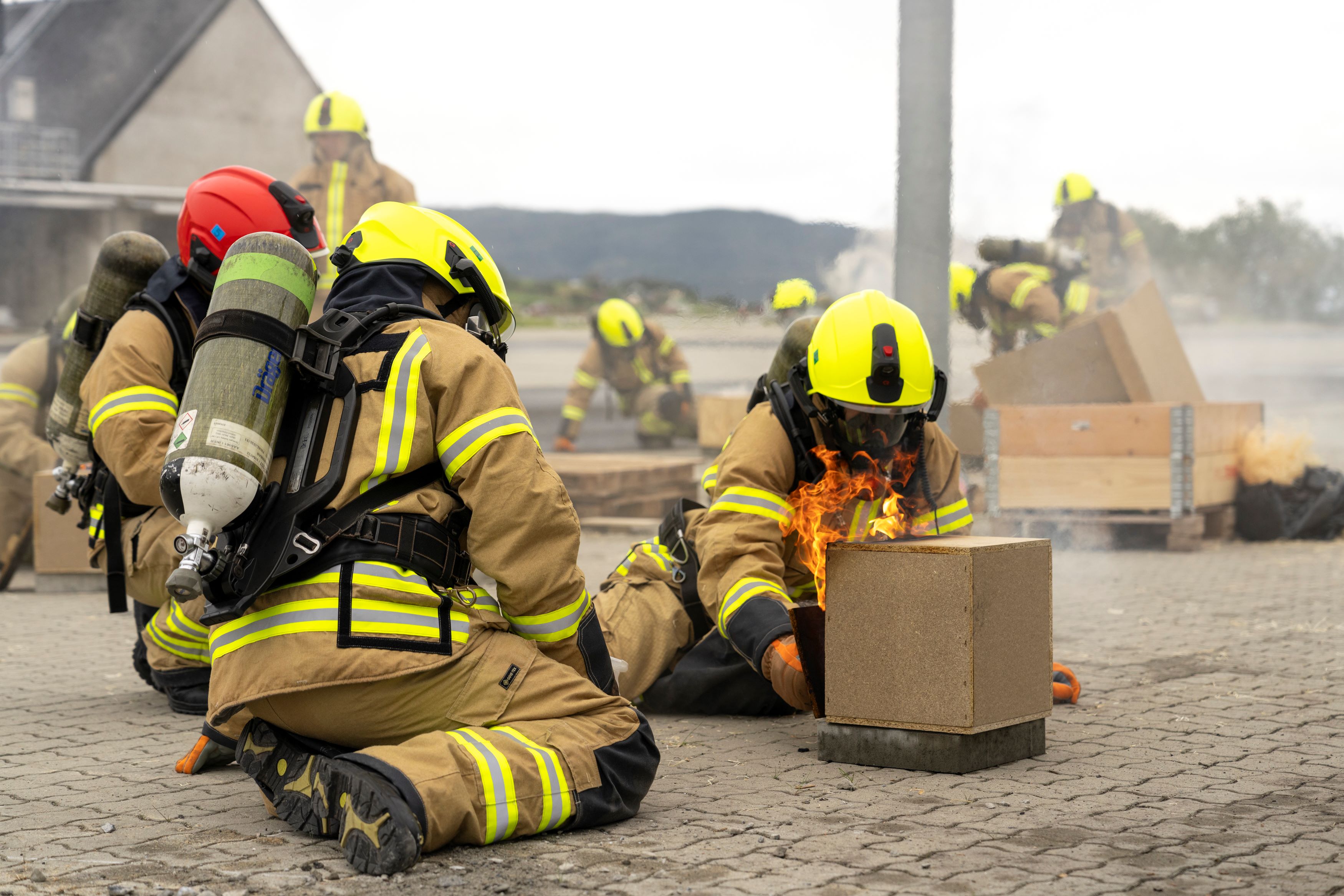 Brannkonstabler sitter på bakken og observerer påtent modellhus