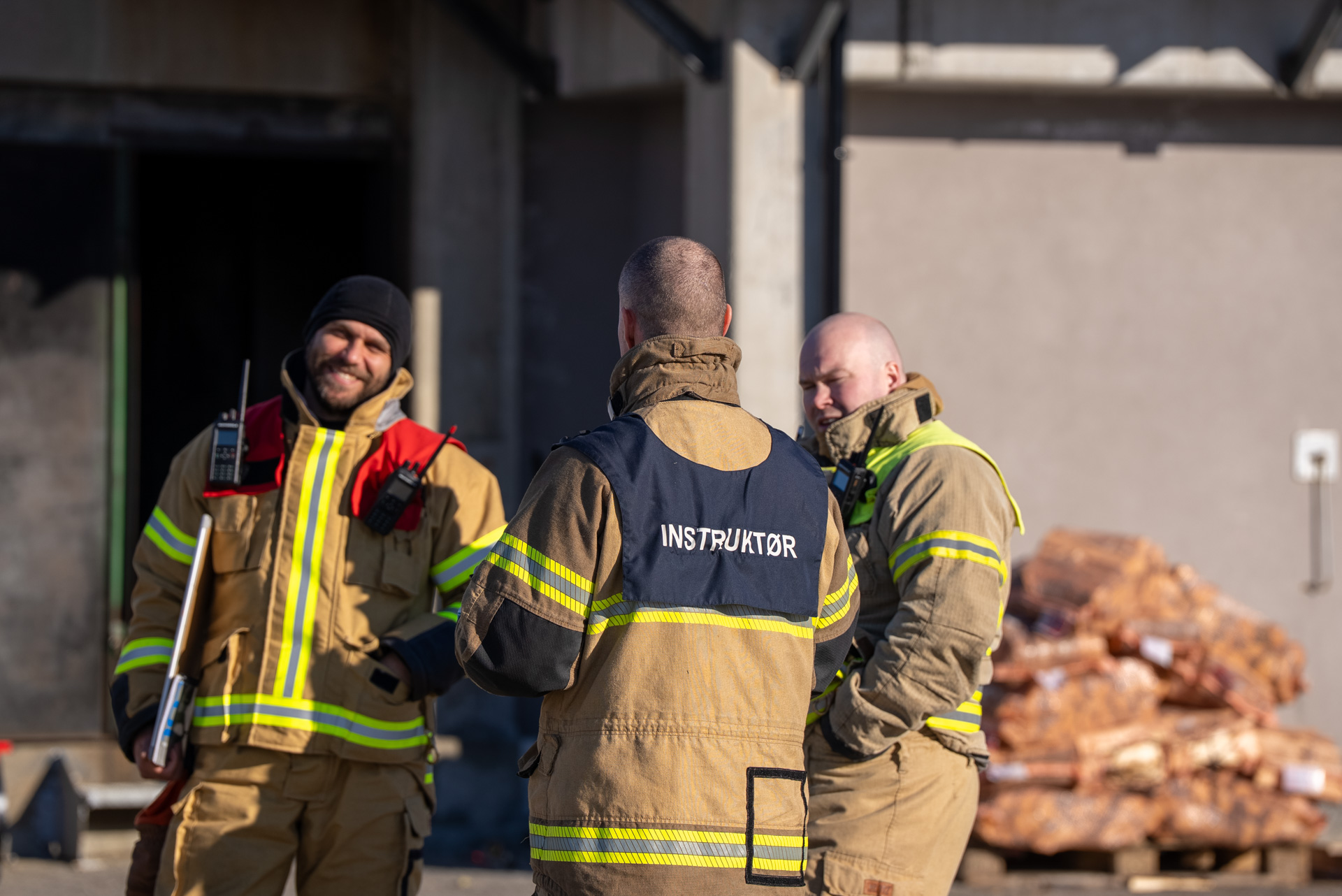 Tre personer i røykdykkerbekledning, to vent mot kamera smilende. foto