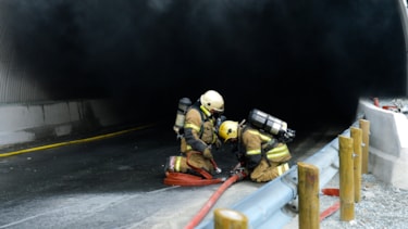 Bilde av to røykdykkere ved inngangen til en tunnel som brenner