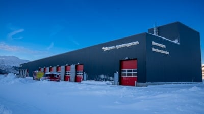 En brannstasjon med røde dører og snø på bakken foran. Himmelen bak er knallblå